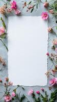 Empty paper surrounded by pink flowers on gray background creating mockup for design photo