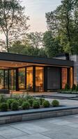 Modern luxury home exterior with illuminated interior at dusk surrounded by lush greenery photo