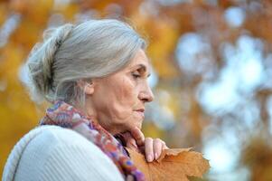 Portrait of beautiful sad senior woman on blurred autumn background photo