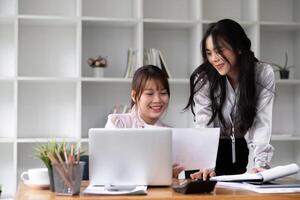 Two Asian businesswomen discuss business planning ideas on work desks in the office. photo