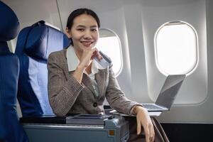 Young Asian woman holding credit card shopping online using website on laptop Sitting near window in first class on airplane during flight, travel and business concept. photo