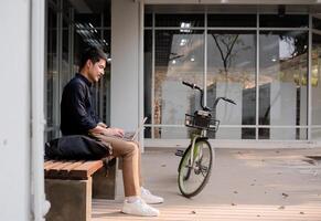 A young Asian businessman rides a bicycle to work. Use a reusable water bottle. Working outside of the office using a laptop The concept of saving energy and reducing pollution to the environment. photo