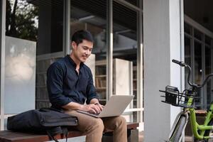 A young Asian businessman rides a bicycle to work. Use a reusable water bottle. Working outside of the office using a laptop The concept of saving energy and reducing pollution to the environment. photo