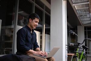 A young Asian businessman rides a bicycle to work. Use a reusable water bottle. Working outside of the office using a laptop The concept of saving energy and reducing pollution to the environment. photo