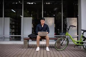 A young Asian businessman rides a bicycle to work. Use a reusable water bottle. Working outside of the office using a laptop The concept of saving energy and reducing pollution to the environment. photo