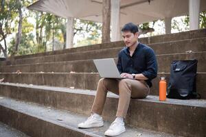 A young Asian businessman rides a bicycle to work. Use a reusable water bottle. Working outside of the office using a laptop The concept of saving energy and reducing pollution to the environment. photo