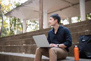 A young Asian businessman rides a bicycle to work. Use a reusable water bottle. Working outside of the office using a laptop The concept of saving energy and reducing pollution to the environment. photo