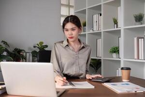 Young Asian business woman sitting in the office using a calculator to calculate business numbers. photo