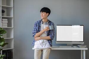Young Asian student smiling happily at computer with blank screen on table photo