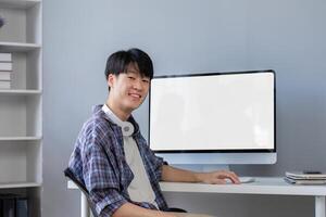Young Asian student smiling happily at computer with blank screen on table photo