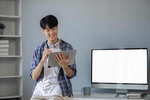 Young Asian student smiling happily at computer with blank screen on table photo