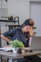 Asian businesswoman feeling tired and stressed over an unsuccessful business while working in a home office decorated with soothing green plants. photo