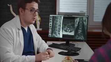An experienced doctor, osteopath, conducts consultations in a modern clinic. A man consults a patient. The MRI image is open on the computer screen. video
