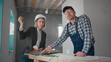 A female architect and a male builder are discussing the finishing options of the premises at the construction site. A representative of the developer monitors the progress of the work video