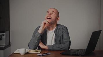 A middle-aged man sits at home, lost in thought, with a dreamy expression on his face. He appears to be reflecting or imagining something. video
