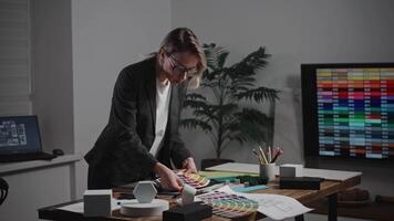 A woman interior designer is creating a mood board. The specialist is using palettes, as well as texture and material samples. The woman is working in a design studio. The office video