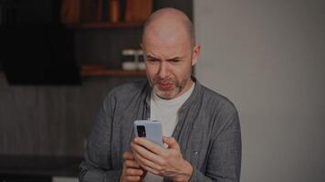 A middle-aged man is in his kitchen, looking at his smartphone screen with a disgusted expression. His face reflects strong aversion to the content he is seeing. video
