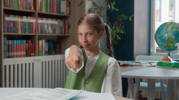 Cute happy smiling Caucasian little child school girl kid student schoolgirl learner pupil looking at camera pointing index finger you calling beckoning inviting hand gesturing in classroom education video