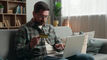Confused adult man male guy shopping laptop at home couch payment online buying internet purchase holding credit card web money e-commerce using computer problem failure unsuccessful transaction error video