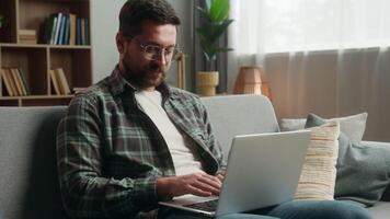 Smiling satisfied Caucasian adult man male guy shopping laptop at home couch playing game online buying internet purchase web browsing working distant computer website showing thumb up like recommend video