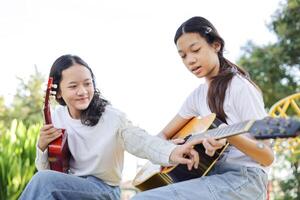 Asian kid girl learning play guitar with friend in the park, Group of friends playing guitar in park photo