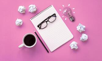 Notebook, coffee cup, glasses and crumpled paper on pink background photo