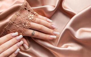 Female hands with pink nail design on silk and lace background photo