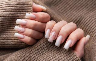 Woman showing stylish white manicure on brown knitted sweater photo