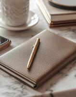 Golden pen lying on leather notebook with smartphone on marble desk photo