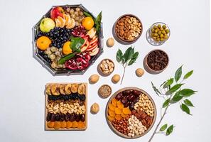 many different trays and bowls with traditional treats for the Tu Bi shvat. top view. white background. flat lay. green branches of the tree. photo