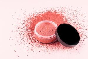 An open transparent cosmetic jar of pink-tone dry blush stands on a loose pink blush swatch. white background. A copy space. texture sample. photo