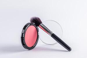 Front view of a beautiful open round pack of pink blush with a professional black makeup brush on it. white background. Product layout. A copy space. photo