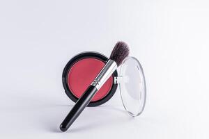 A beautiful professional black makeup brush leaned on a open round package with pink blush. Front view. white background. layout. product advertising. photo
