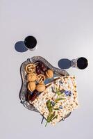 matzoth on a silver tray with nuts, dates on a light background. glasses with red wine. A traditional treat for the Passover holiday. top view photo