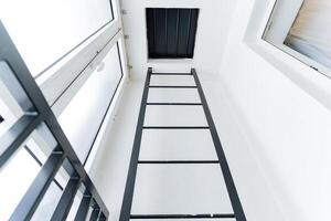 A ladder made of composite material going up against the parallel facade of a building with rectangular glass windows in a room. photo