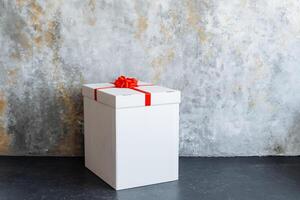 A white rectangular gift box with a red bow rests on a table photo