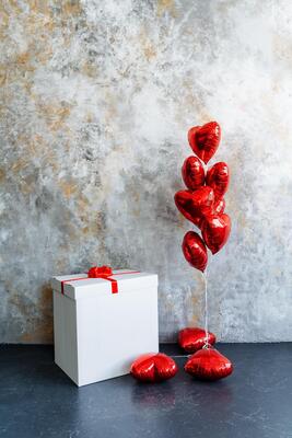 a white box with a red ribbon and a bunch of red balloons in the shape of hearts