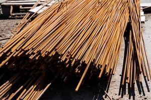 Closeup of rusty steel rebars at construction site creating a textured pattern. The heavy metal rods stack in an angled pile, providing reinforcement for the buildings foundation photo