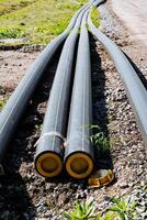 Industrial black pipes laid on the ground at a construction site for infrastructure development. Closeup view of the installation in a landscape with gravel and vegetation photo