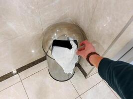 The individual disposes of a toilet paper roll in the bathroom trash can, located on the floor. photo