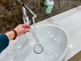 A person uses a plumbing fixture sink to wash their hands using liquid water with the gesture of activating the tap. photo