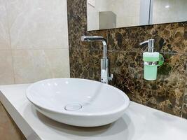 Plumbing fixture with a rectangle-shaped sink, tap, and soap dispenser for the bathroom interior design made of wood. photo
