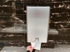 A person picks up a napkin from a dispenser filled with paper towels made of various materials like wood, metal, and composite. photo
