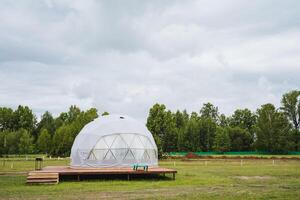 A unique geodesic ecofriendly transparent dome in a green field, perfect for ecotourism and glamping. It provides a pioneer landscape for a peaceful retreat in nature photo