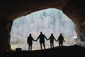 A group of individuals is standing together in a dimly lit cave, all holding hands in a circle, creating a sense of unity and togetherness amidst the stunning natural surroundings photo