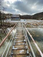 A beautiful wooden bridge gracefully spans a peaceful river, with a charming house nestled in the background, creating a picturesque winter scene adorned with snow and ice photo