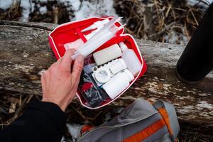 A person confidently holds a wellstocked first aid kit right next to their backpack, fully prepared for any unforeseen emergencies that might arise during their exciting adventures photo