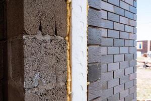 During construction, a building wall is being enhanced with insulating foam and brick to boost thermal efficiency and structural integrity, improving energy efficiency photo