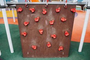 In a cheerful, lively playground, a vibrant climbing wall adorned with bright red holds captivates children, promoting fitness, social interaction, and essential life skills through play photo
