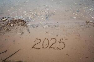 The year 2025 is gently etched in fine sand on a stunning beach, where the persistent ocean waves will slowly and gradually erase those delicate numbers over the passage of time photo